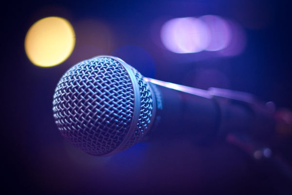 A vocal microphone in close-up against purple and gold stage lights.