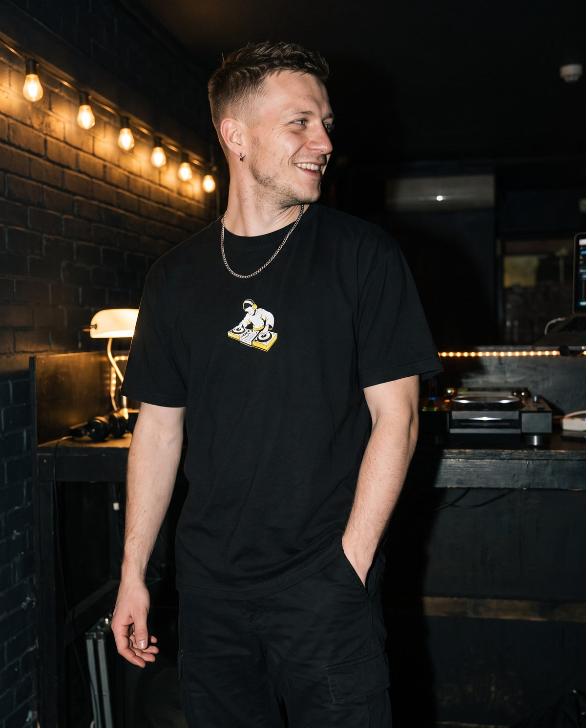 Model wearing the On The Decks t-shirt in Black, behind a DJ booth