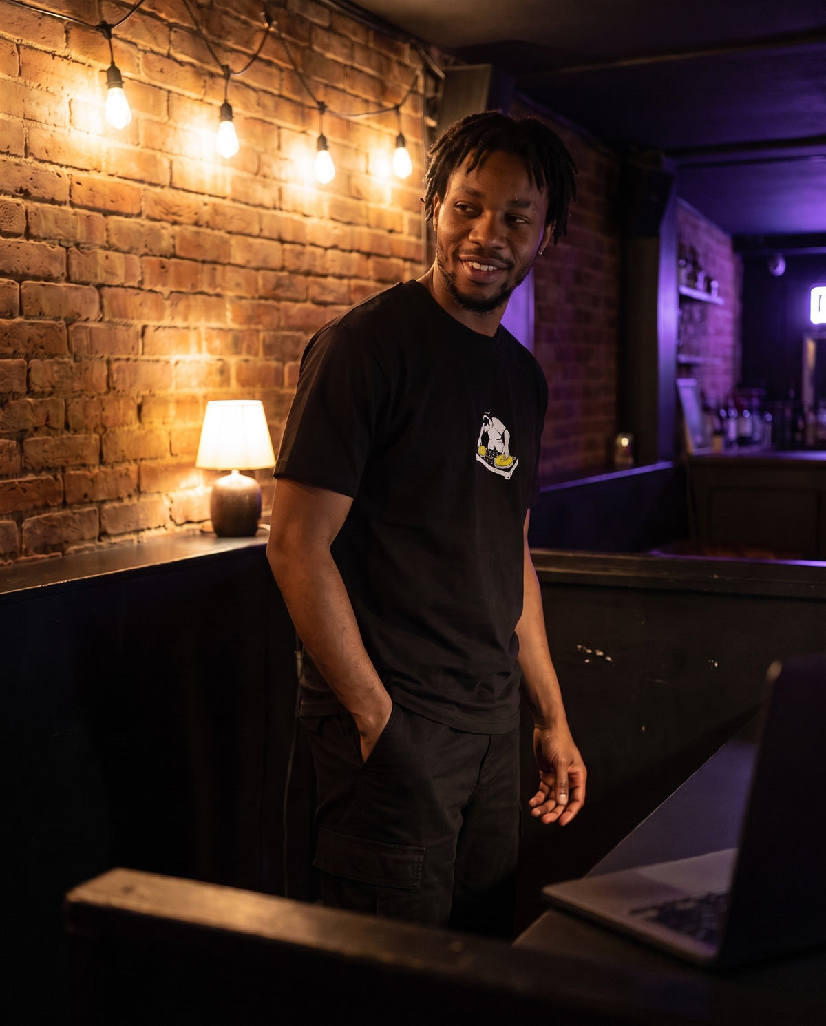 Model wearing the Turntablist t-shirt in Black, behind a DJ booth