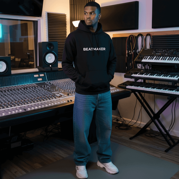 Producer in a Beatmaker hoodie standing in a home studio beside monitors and a keyboard