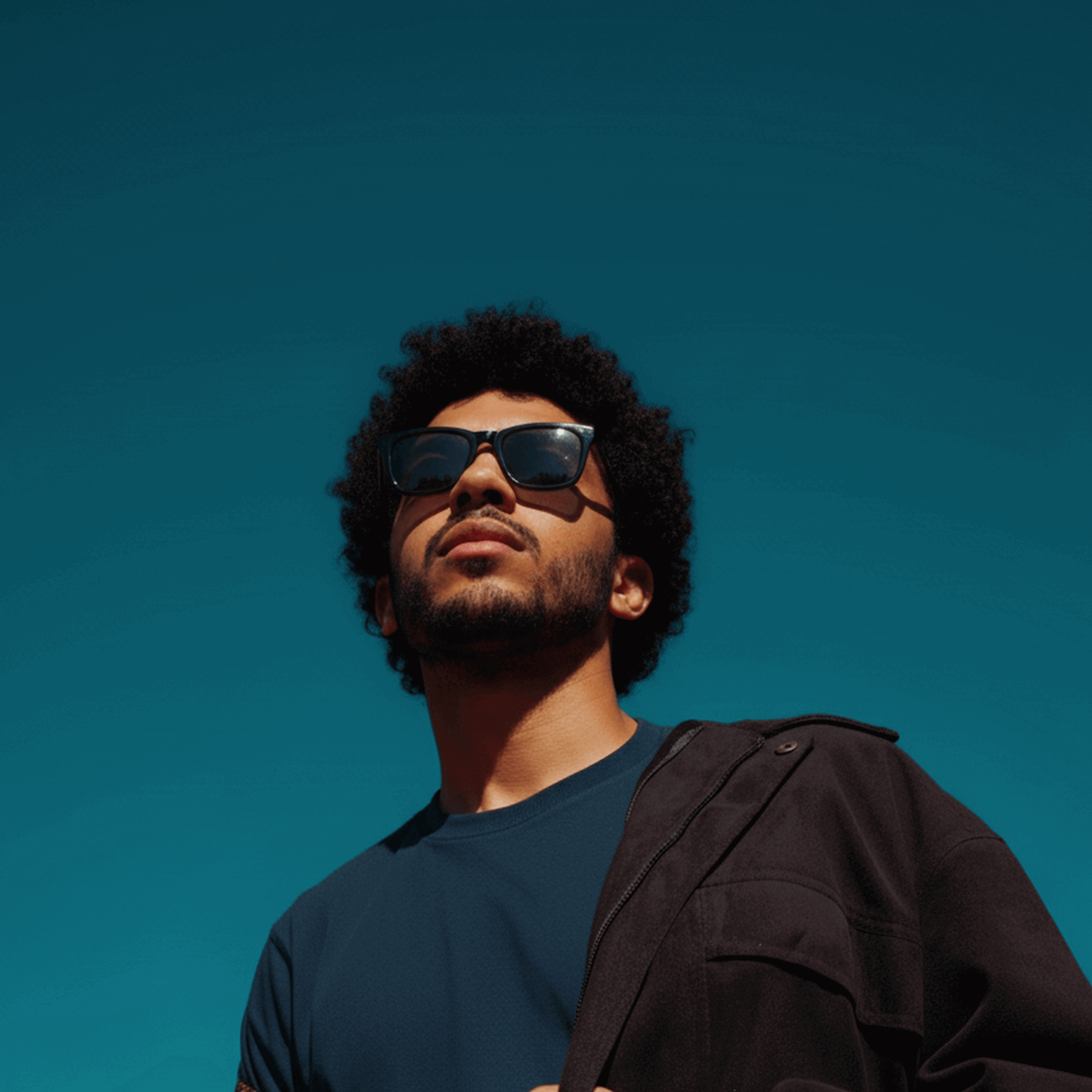 Man wearing sunglasses and hip hop clothing against a clear blue sky