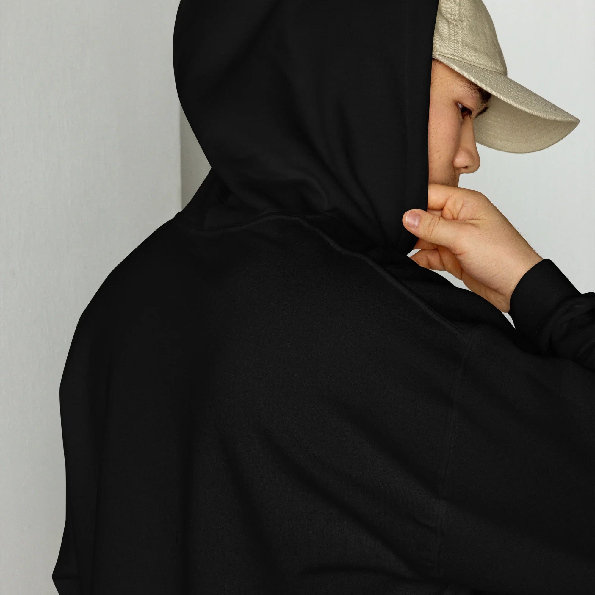 Person wearing a black hoodie and beige cap against a plain background