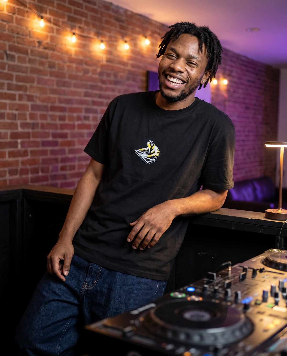 Model wearing the Cut & Scratch t-shirt in Black, behind a DJ booth