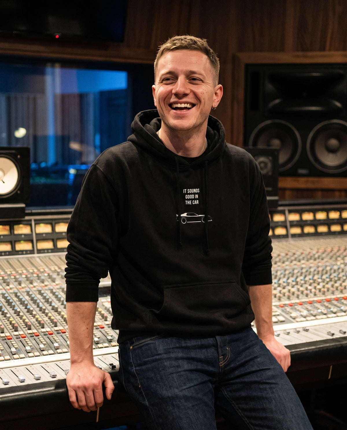 Model wearing the Sounds Good In The Car hoodie in Black, in a recording studio control room